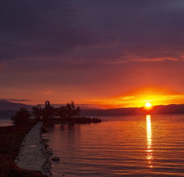 Denizde gün doğumu eski bir kilisenin siluetinde. Kızıl gökyüzü