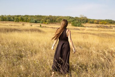 Siyah elbiseli güzel, koyu renk saçlı kadın sahada duruyor. Sahadaki güzel kız özgürlüğün tadını çıkar.
