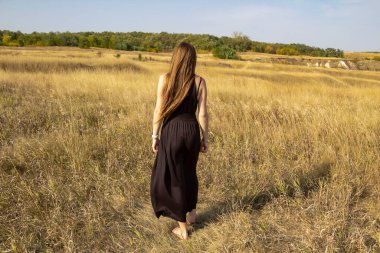 Siyah elbiseli güzel, koyu renk saçlı kadın sahada duruyor. Sahadaki güzel kız özgürlüğün tadını çıkar.