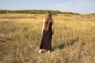 Siyah elbiseli güzel, koyu renk saçlı kadın sahada duruyor. Sahadaki güzel kız özgürlüğün tadını çıkar.