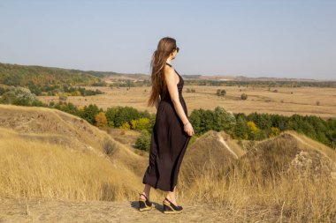 Siyah elbiseli güzel, genç, siyah saçlı kadın sahada duruyor. Sahadaki güzel kız özgürlüğün tadını çıkar.