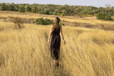 Siyah elbiseli güzel, genç, siyah saçlı kadın tarlada yürüyor. Sahadaki güzel kız özgürlüğün tadını çıkar.
