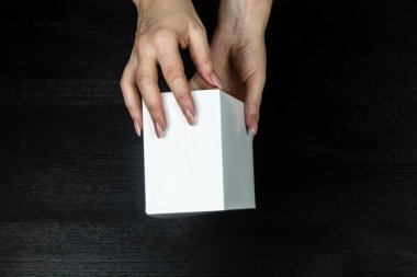 Kadın elleri tahta arka planda beyaz bir kutu tutuyor.