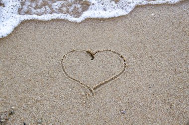 Kumsalda kumların üzerinde dalgalar ve kumların üzerinde bir kalp var. Dalgaların güzel manzarası