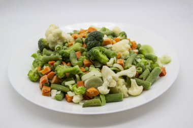 Donmuş sebzeler: karnabahar, yeşil bezelye, pırasa, brokoli, havuç, beyaz tabakta yeşil fasulye..