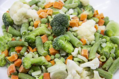 Donmuş sebzeler: karnabahar, yeşil bezelye, pırasa, brokoli, havuç, beyaz tabakta yeşil fasulye..