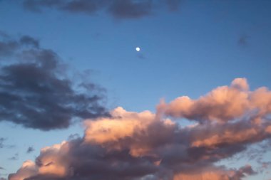 Mavi gökyüzünde güzel, koyu bulutlar ve arka planda ay var.