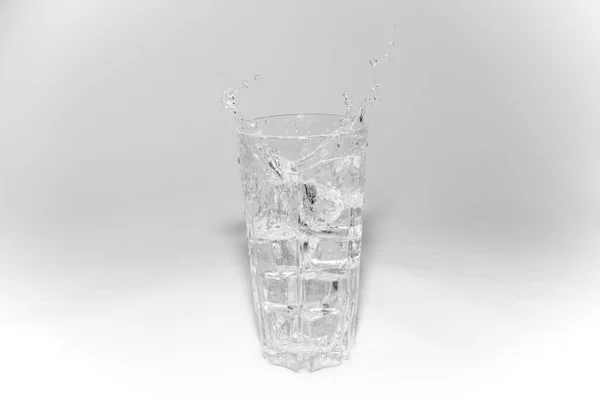 Spruzzi d'acqua in un bicchiere con ghiaccio su sfondo bianco — Foto Stock
