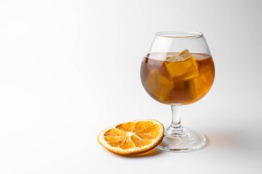 Bir bardak buzlu viski ve beyaz arka planda bir dilim portakal.
