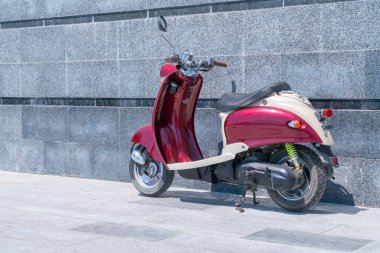 Taştan bir duvarın karşısında duran kırmızı bir scooter.