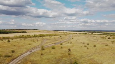 Sonbahar tarlaları arasında toprak bir yol ve yüksek bulutlarla dolu mavi bir gökyüzü.