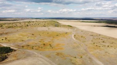 Sonbahar tarlaları arasında toprak bir yol ve yüksek bulutlarla dolu mavi bir gökyüzü.