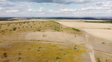 Sonbahar tarlaları arasında toprak bir yol ve yüksek bulutlarla dolu mavi bir gökyüzü.