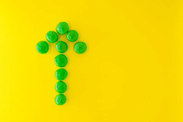 Groene pijl van chocolade snoep op gele achtergrond met kopieerruimte voor tekst, platte lay. — Stockfoto