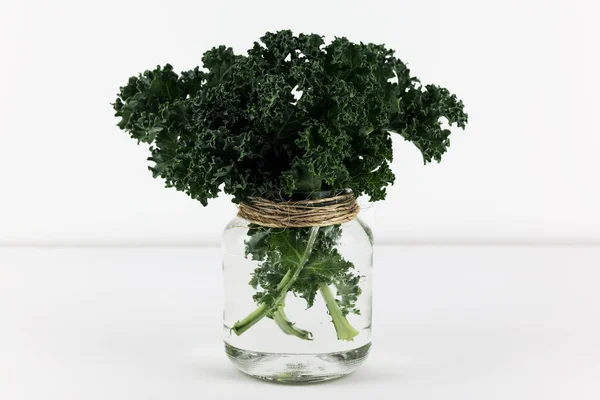 Curly green kale leaves in recycled glass jar.