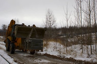 Traktör bir kova üzerinde beton kaldırım taşır.