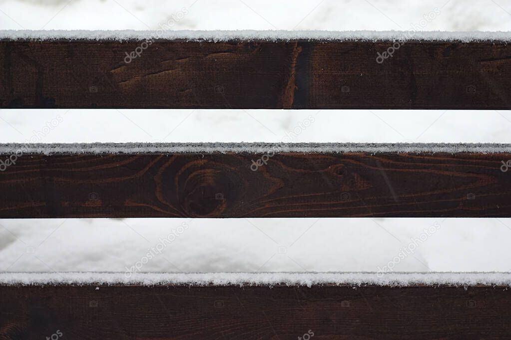 fresh snow on the crossbeams of a wooden bench