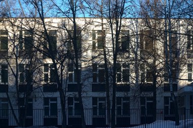 Okul binasının ön cephesi Kışın ağaçların arkasında