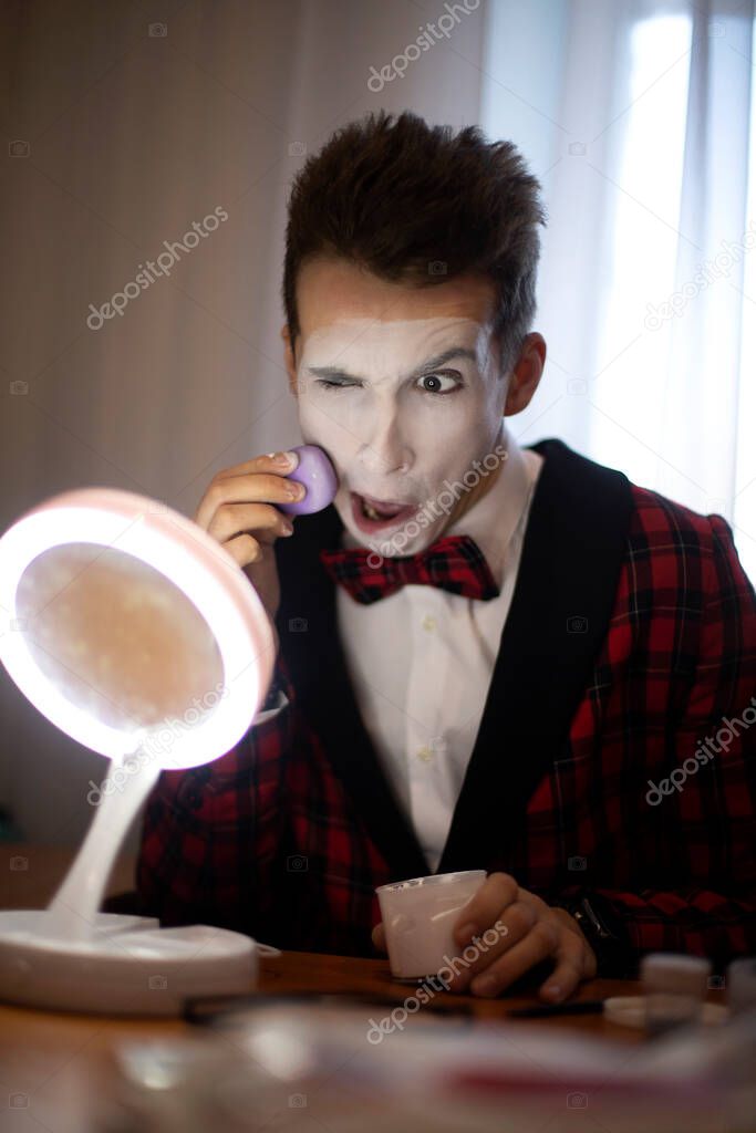 mime puts on makeup in front of the mirror and makes faces