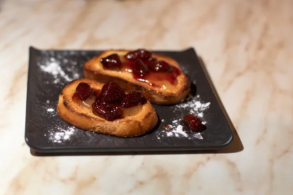 Kahvaltı, çilek reçelli tost ve siyah tabakta bal.