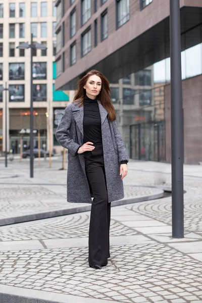 beautiful girl with makeup in a spring coat and trousers posing on the city streets. Woman in formal clothes smiling cute