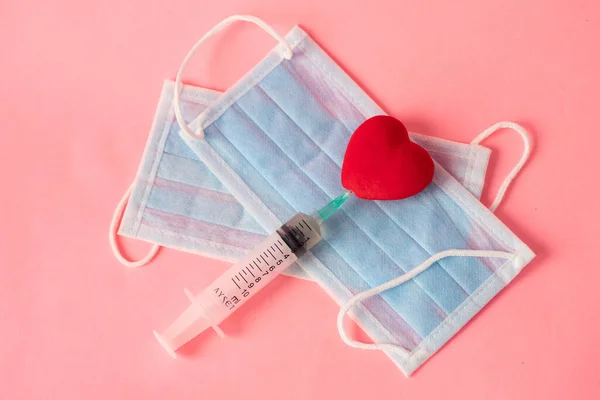 The syringe with the medicine and the heart lie on the medical masks. Love during a pandemic. Valentine\'s Day