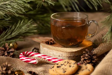 Kumaşın arka planında, jgut çuval bezi ve bir Noel ağacının dalları bir ağaç çayının üzerinde kurabiyelerle ve konili lolipopla duruyor. Akşam atıştırması. Noel Baba için ikramlar