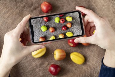 En iyi akıllı telefonu elinde meyve fotoğrafı tutan adamın kırpılmış görüntüsü. Adam telefonda yemeğin fotoğrafını çekiyor. Bir yemek fotoğrafçısı telefonunda elma ve karambola resimleri çekiyor. Meyve. Kollar