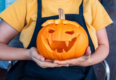 Gülümseyerek oyulmuş Cadılar Bayramı balkabağı ellerindeydi. Azizler Günü