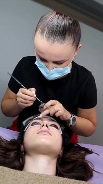Güzellik salonu. Kirpik temizleme işlemi sırasında göz kapağının üst kısmına siyah kirpik boyası sürme ve kirpik düzeltme
