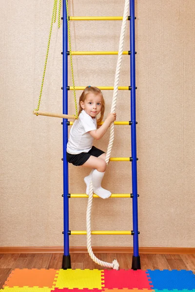 Little girl climbs stairs holding on to rope.