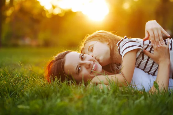 Mother and daughter lying on grass. Kiss