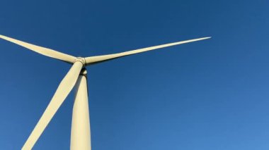 Rüzgar türbinleri elektrik enerjisi üreten pervane çiftlikleri. Rüzgâr değirmeni güç üretimi. Rüzgâr çiftliği türbinleri. Mavi gökyüzü, yenilenebilir sürdürülebilir enerji üretimi ile yeşil bir alanda açan pervaneler.