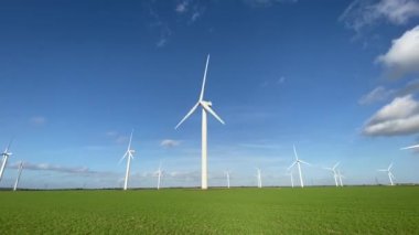 Modern wind turbines stand in a lush green field under a clear blue sky, producing renewable electricity and symbolizing sustainable energy technology. Perfect for concepts of eco power, innovation, and clean environment. video footage