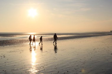 Günbatımında yürüyen insanlar, Winchelsea plajı ile Rye Harbour doğası arasındaki kumsaldaki ıslak kumu yansıtırken Doğu Sussex, İngiltere 'de popüler turist plajını rezerve ederler.