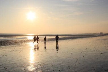 Günbatımında yürüyen insanlar, Winchelsea plajı ile Rye Harbour doğası arasındaki kumsaldaki ıslak kumu yansıtırken Doğu Sussex, İngiltere 'de popüler turist plajını rezerve ederler.