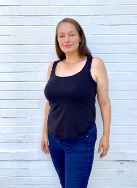 Ayrıca beyaz tuğla duvara karşı yelek ve dar kot giyen kıvrımlı kadın modeli.