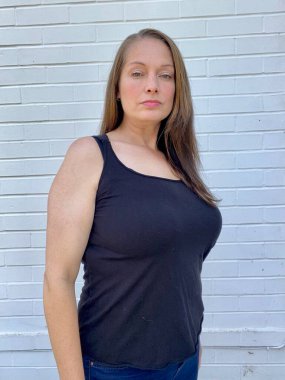 Ayrıca beyaz tuğla duvara karşı yelek ve dar kot giyen kıvrımlı kadın modeli.