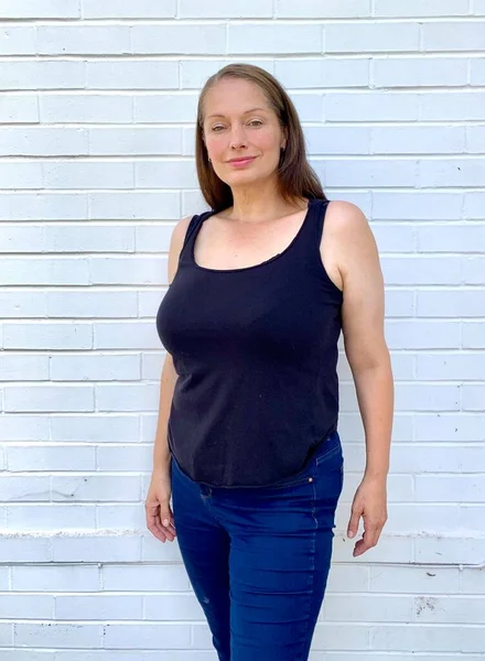 Ayrıca beyaz tuğla duvara karşı yelek ve dar kot giyen kıvrımlı kadın modeli.