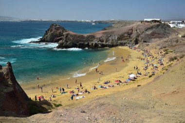 The beautiful Playa de Papagayo in the south west of Lanzarote, Spain. The town Playa Blanca in the background. People on the beach.