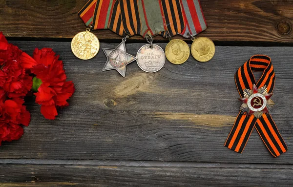 Victory Day.Order of the red star with the Russian inscription Patriotic war and medals on a wooden background with red carnations.Celebration on may 9.Memorial day.Greeting card. copy space