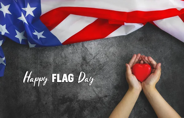Flag Day.Greeting card. American Flag next to childs hands holding red heart- symbol of gratitude and love for Memorial Day or 4th of July.