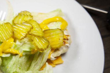 Marul, hardal ve dilimlenmiş kazmalarla kaplı ızgara tavuk göğsü.