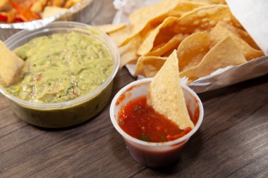 Salsa soslu tortilla cipsi ve arka planda paket paket paket mısır cipsinin yanında guacamole.