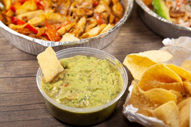 Guacamole soslu tortilla cipsi yanında açık cips ve teneke kutuda iki paket yemek.