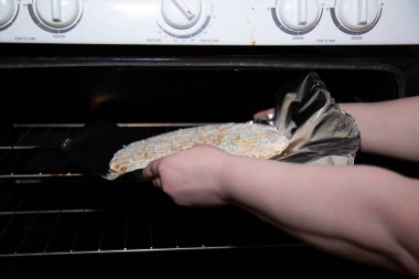 Donmuş peynirli pizzayı fırına koyan bir kadının ellerini kapatın.