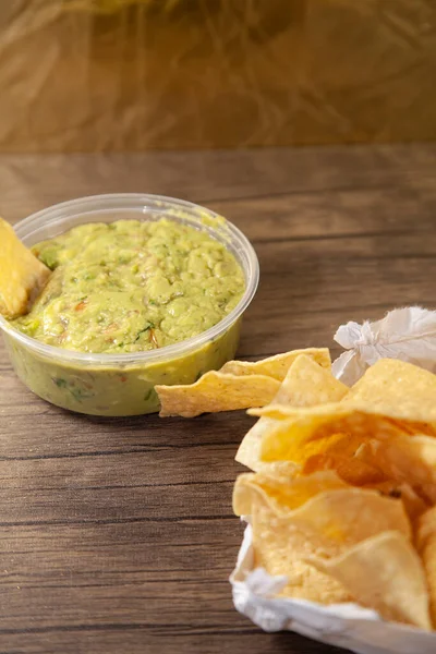 Tortilla chip in guacamole next to a bag of chips