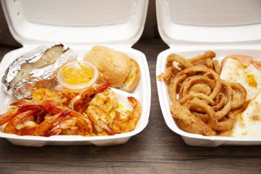 Izgara karides, fırında patates ve yanında beyaz bir köpük havrut kutusunda bir kutu sos ve yanında da Quesadilla ve soğan halkası yemeği.