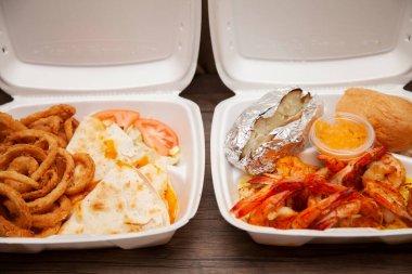 Izgara karides, fırında patates ve yanında beyaz bir köpük havrut kutusunda bir kutu sos ve yanında da Quesadilla ve soğan halkası yemeği.