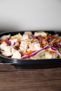 Izgara tavuk, pastırma, marul, lahana, dilimlenmiş peynir ve paket servis kutusunda doğranmış domates salatası.